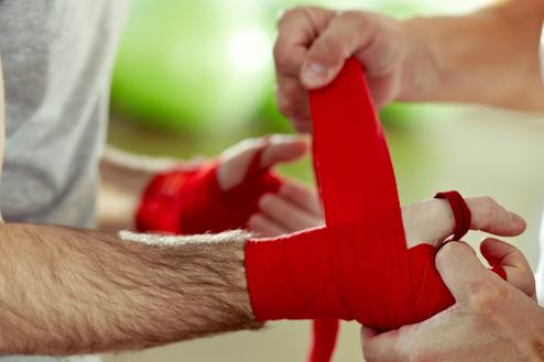 Hände eines Mannes wickeln rote Handbandagen um die Hände eines anderen Mannes in einem Trainingsraum.